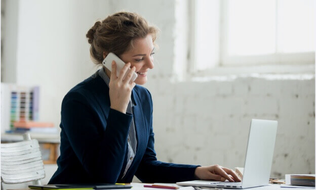 Smiling woman talking on phone and working on computer